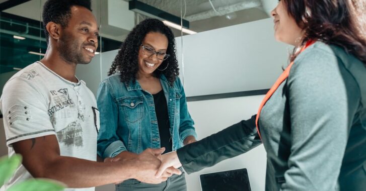 Smiling couple shaking hands with advisor in modern office.