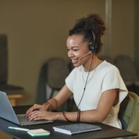 African American woman in a call center setting, working on a laptop and wearing a headset.