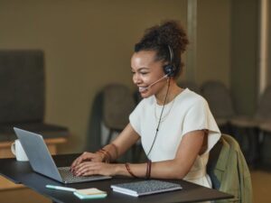 African American woman in a call center setting, working on a laptop and wearing a headset.