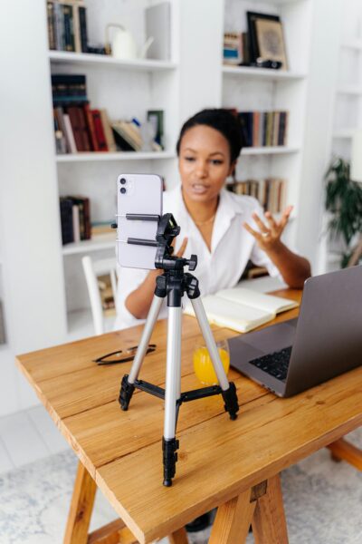 A professional woman conducts a virtual meeting using a smartphone on a tripod in a home office.